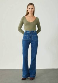 Roheline pika varrukaga top ja kõrge vöökohaga sinised lehvikudega teksad, millel on kaks esist pocketit, kontrastsete õmbluste ja siledaga.