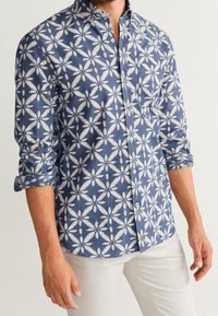 Camisetta a maniche lunghe con motivo floreale in blu navy e bianco, realizzata in tessuto intrecciato. Presenta maniche arrotolate e colletto classico.
