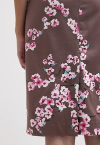 Brun kjole med et blomsterprint af lyserøde og hvide blomster, glat tekstur og tætsiddende design. Slutter lige over knæet.