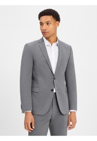 Grijze blazer gemaakt van gestructureerde stof, voorzien van een enkele knoop, revers en een borstzak, gecombineerd met een witte shirt.