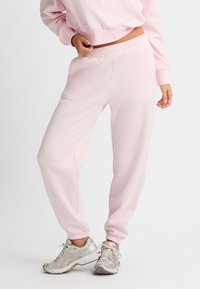 Helle rosa Jogginghose mit lockerem Schnitt, elastischem Bund und gerippten Knöcheln. Verfügt über ein minimales Branding in passender Farbe.