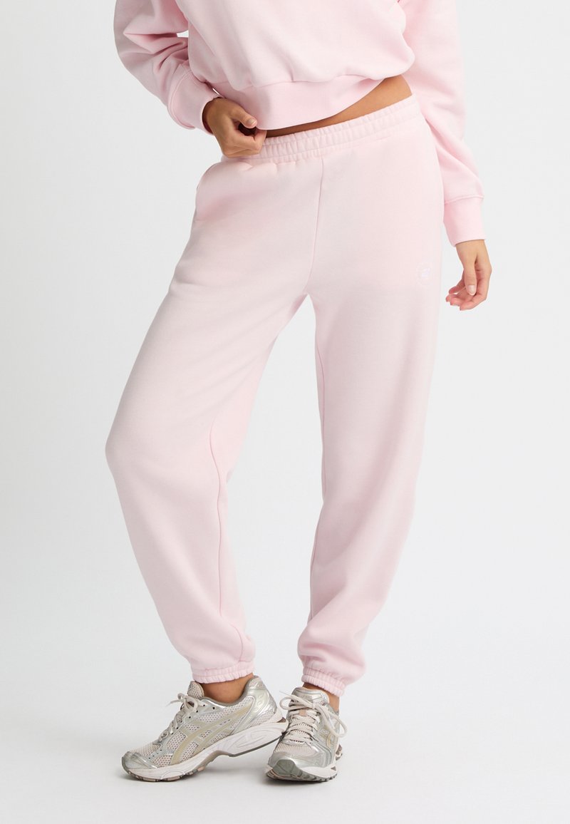 Helle rosa Jogginghose mit lockerem Schnitt, elastischem Bund und gerippten Knöcheln. Verfügt über ein minimales Branding in passender Farbe.
