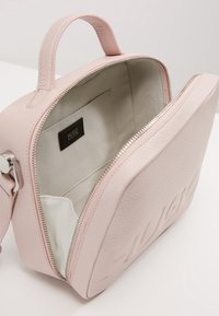 Borsa a mano in pelle rosa con logo impresso, chiusura con zip, manici doppi e un interno in tessuto morbido. L'interno presenta un'etichetta e una tasca.