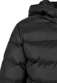 Giacca piumino nera trapuntata con cuciture orizzontali e colletto imbottito vista dalla parte posteriore della spalla.