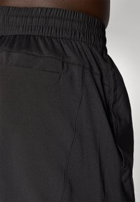 Sorte sportshorts lavet af glat stof, med en elastisk talje og en baglomme, der har et strømlinet design og minimal tekstur.