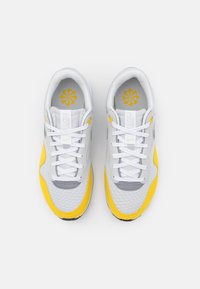 Sneakers med en grå mesh-överdel, gula accenter och vita snören. Gummisula med ett texturerat mönster. Logodetalj på tungan och innersulan.