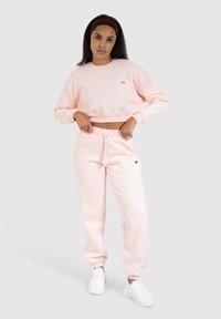 Roze katoenen crewneck sweatshirt met bijpassende taps toelopende sweatpants, beide met een subtiele textuur en logo, gecombineerd met witte sportschoenen.