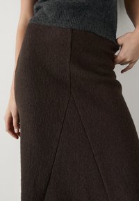 Ruskea villasekoitekangas hame, jossa on teksturoitu pinta, sivuhaarukalla ja vartalonmyötäisellä siluetilla, täydentäen ylleen pukeutunutta harmaata villapaitaa.