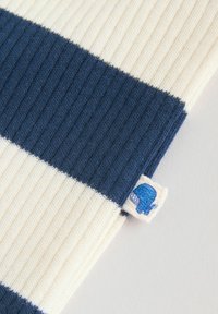 Közeli kép bordázott anyagról, rajta széles sötétkék és fehér vízszintes csíkokkal, valamint egy kis címkével, amin egy kék csiga illusztráció látható.