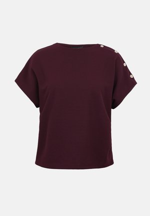 Dunkellila Bluse mit kurzen Ärmeln, rundem Ausschnitt und vier dekorativen, metallischen Knöpfen entlang der linken Schulter.