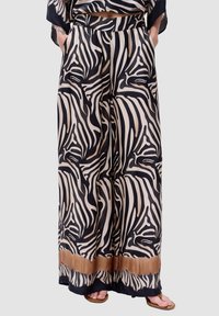 Brede pijpen in zwart en beige zebra print. Gemaakt van gladde stof met een gevlochten tailleband en een bruine verloopaccent aan de zoom.