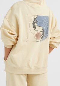 Felpa leggera color beige chiaro con polsini e orlo a costine. Sul retro presenta una grafica di due silhouette contro onde blu e un'esplosione di sole rossa. Include il logo O'Neill.