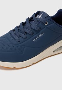 Baskets bleu marine avec surface texturée, design à lacets et logo « SKECHERS » blanc. Comprend une semelle en caoutchouc légère et des trous de ventilation.