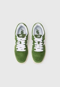Zelene antilop cipele s bijelim vezicama, perforiranim detaljima i kremastom gumiranom potplatom. Sadrži "New Balance" logotip na jeziku.