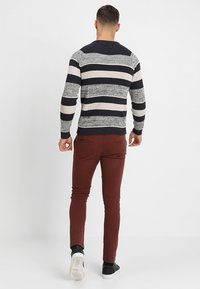 Sweter dziany w granatowe, kremowe i szare poziome paski. Połączony z bordowymi spodniami dresowymi i czarnymi trampkami z białymi podeszwami.