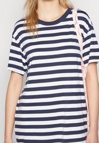 Laivastonsininen ja valkoinen raidallinen t-paita, jossa on lyhyet hihat, pyöreä pääntie ja rento leikkaus. Materiaalina pehmeä puuvillakangas. Mukana vaaleanpunainen vaunun hihna.