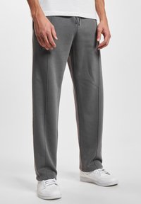 Grå sweatpants lavet af et blødt stof, med en snor i taljen, sidesømme og en afslappet pasform, parret med hvide sneakers.