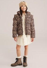 Leopardų rašto pūkinė striukė, smėlio spalvos marškinėlių suknelė ir atitinkami leopardų rašto lace-up batai. Minkšta tekstūra, su kapišonu ir pūsta siluetu.