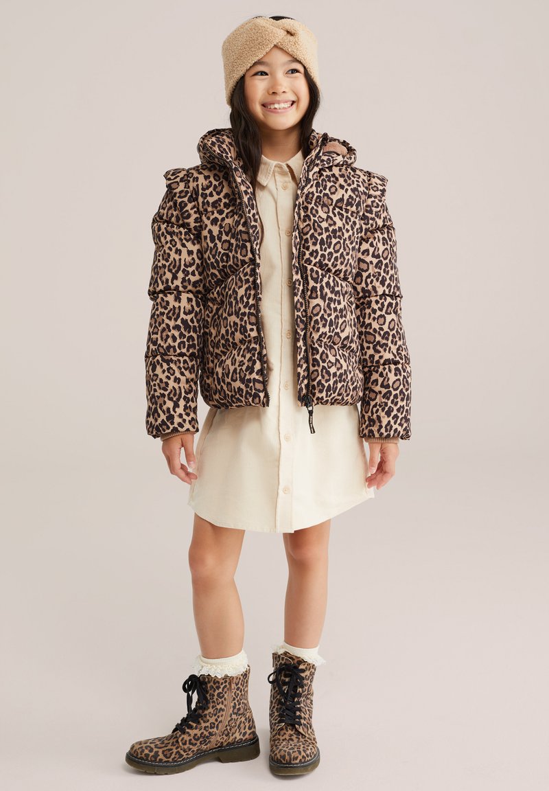 Leopardų rašto pūkinė striukė, smėlio spalvos marškinėlių suknelė ir atitinkami leopardų rašto lace-up batai. Minkšta tekstūra, su kapišonu ir pūsta siluetu.