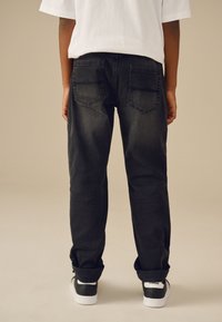 Jean en denim noir à coupe droite, avec poches arrière et légère décoloration. Associé à des baskets noires et blanches.