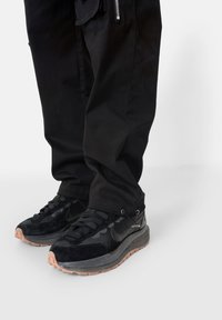 Zapatillas deportivas negras con una mezcla de materiales de malla y ante, que cuentan con una suela texturizada y sutiles acentos de marca.