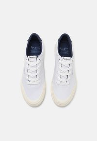 Valkoinen alhaisen varren sneakers -pari, jossa on valkoiset nauhat ja vaaleanbeige kumipohjat, tummansininen sisävuori sekä "Pepe Jeans London" -brändäys kengän kielekkeessä ja sisäpohjassa.