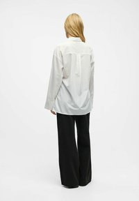 Chemise blanche à rayures avec col et manches longues, assortie à un pantalon noir ample. La chemise présente un empiècement et une coupe décontractée.