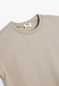 Lys beige bomuldstrøje med ribbet rund halsudskæring og blød tekstur. Etiket med teksten "Koton Kids" nær halsudskæringen. Enkel og ren design.