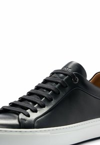 Baskets en cuir noir à finition lisse, avec des lacets plats, un bout arrondi et une semelle en caoutchouc blanche. Détail discret de logo près des lacets.