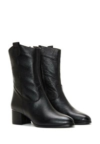 Botines de cuero negro con un acabado texturizado, que presentan una punta afilada y un tacón cuadrado, diseñados con pequeñas lengüetas y cremalleras laterales.