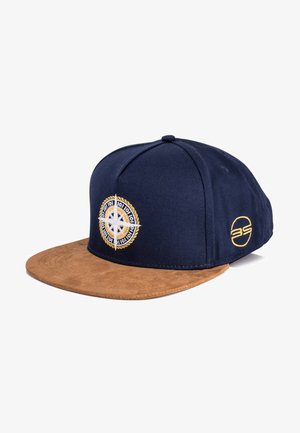 Navy blue baseball cap with a tan suede brim. Features an embroidered compass design and a circular logo on the side.
