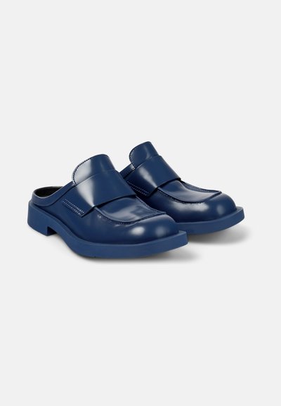 Navy blue slip-on clogs with a glossy finish, featuring a wide strap and stitched detailing, on a textured sole.