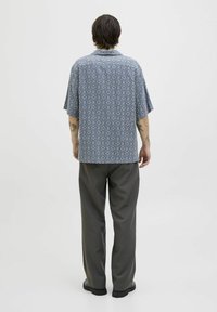 Camisa de manga corta con un diseño de diamantes en azul y blanco, combinada con pantalones grises de corte holgado y zapatos negros.