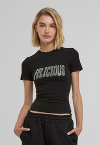 Svart åtsittande t-shirt med ordet "FELICIOUS" i silverpaljetter över framsidan, med kort ärm och rund halsringning.