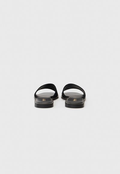 Svarte flate sandaler med en glatt skinnoverdel, åpen tå og et minimalistisk design. Har en subtil sømdetaljering langs sålen.