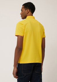 Geel polo-shirt met een kraag, korte mouwen en zijsplitten. Zacht katoenen materiaal met een gladde textuur. Heeft een achterste yoke-detail.