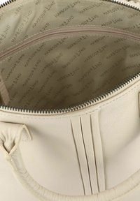Interior de un bolso de piel beige que muestra una textura suave, con un bolsillo con cremallera y un patrón de logotipo en relieve repetido en el forro de tela.
