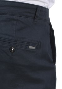 Shorts bleu foncé en coton avec une texture lisse. Comprend une fermeture à bouton, une poche latérale et un accent en tissu rayé.