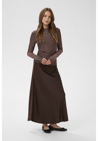 Ruskea pitkähihainen yläosa, jossa kiiltävä pinta, yhdistetty tummanruskeaan satiinihameeseen ja mustiin tasapohjaisiin kenkiin. Yksinkertainen ja tyylikäs muotoilu.