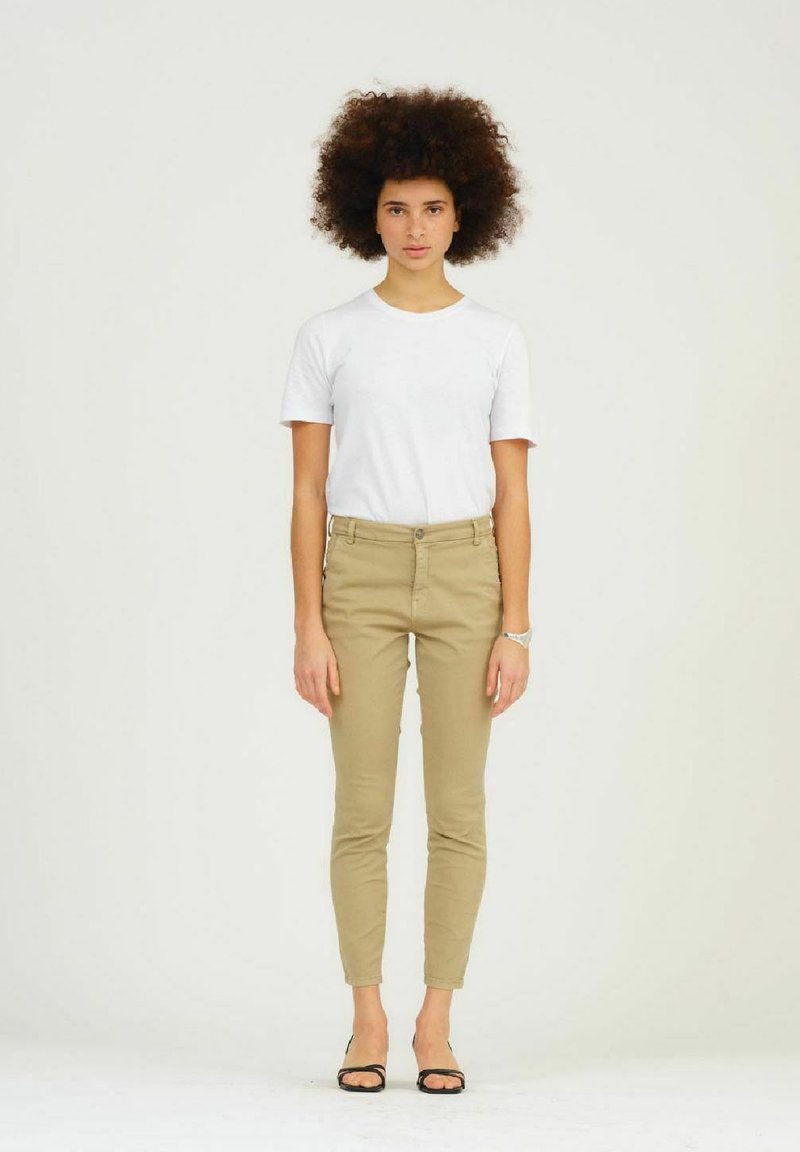 Kaki slim-fit broek met zijzakken en knoopsluiting, gecombineerd met een witte shirt met korte mouwen. Model staat voor een neutrale achtergrond.