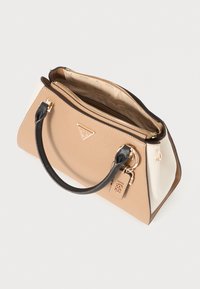 Borsa Guess beige e bianca con manici neri, dettagli dorati, chiusura zip e un portachiavi del 1981 su sfondo bianco.