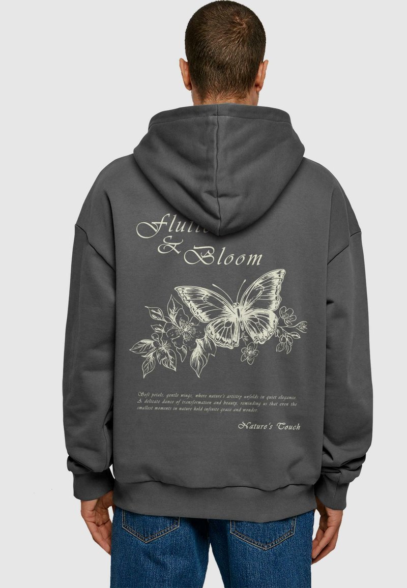 Mørkegrå hættetrøje med et stort hvidt sommerfugle- og blomsterdesign på ryggen, samt dekorativ tekst nedenfor.