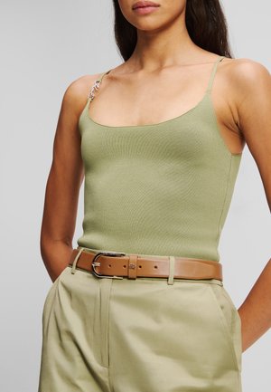 Olivengrønn ribbestrikket tank top med smale stropper og dekorativt sølvfarget beslag, kombinert med beige bukser med belte som har en glatt tekstur.