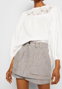 Hvid bluse med teksturerede prikker og blonde detaljer. Rutig shorts i pastelfarver med frontlommer og knaplukning.