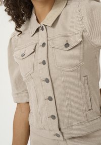 Beige-raitainen farkkutakki, jossa on lyhyet hihat, etutaskut, harmaat napit ja kauluksellinen pääntie. Pinnassa on havaittavissa tekstuuri.