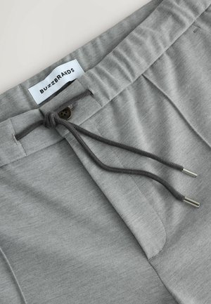 Graue Baumwoll-Jogginghosen mit einem Kordelzugbund, mit einem Knopfdetail und feiner Textur. Das Etikett trägt die Aufschrift "BUZZBRANDS."