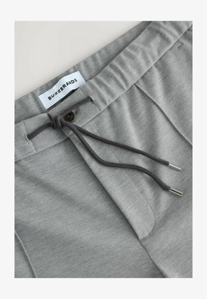 Gray cotton joggers with a drawstring waist, featuring a button detail and subtle texture. Label reads "BUZZBRANDS."
