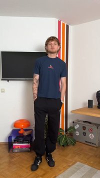 T-shirt azul-marinho de mangas curtas com um pequeno bordado, combinado com calças pretas de corte descontraído e tênis pretos. Visual simples e moderno.