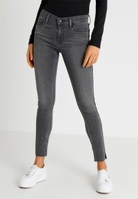 Jeans ajustados grises de talle alto, con un clásico diseño de cinco bolsillos y un sutil detalle de abertura lateral. Combinados con zapatillas blancas.