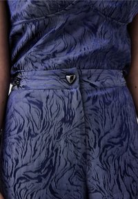 Robe bleue à motifs présentant un design texturé avec des lignes fluides, une taille cintrée et une fermeture à bouton métallique en forme de cœur.